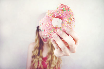 Woman holding donut while standing wall