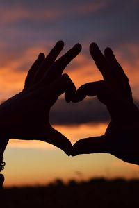 Close-up of hand holding heart shape against sky during sunset