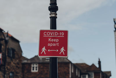 Road sign by buildings in city against sky