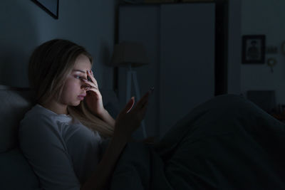 Sleepy exhausted woman lying in bed using mobile phone, touching forehead, can not sleep. insomnia