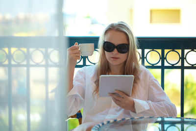Young woman using digital tablet while having coffee in balcony