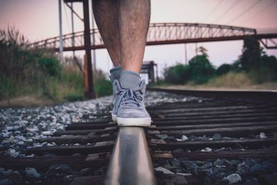 Low section of man walking on railroad track against sky during sunset