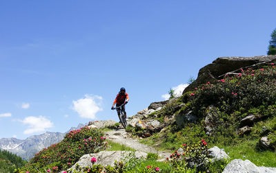 Low angle view of mid adult man riding bicycle on hill against blue sky