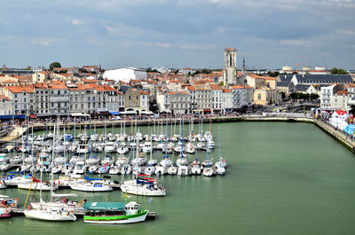 Sailboats moored in harbor against buildings in city