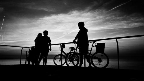 Silhouette people with bicycles standing by sea at observation point