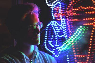 Close-up of young man looking at illuminated lighting equipment in darkroom