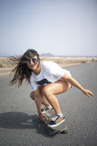 Woman with tousled hair skateboarding on sunny day