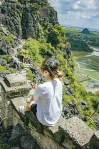 Rear view of woman sitting on rock
