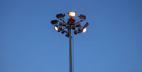 Low angle view of illuminated floodlights against clear blue sky