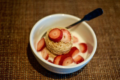 High angle view of shredded wheat and strawberries with milk in bowl on table