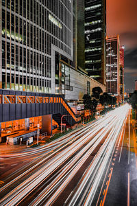 Light trails on road by buildings in city at night