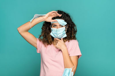 Portrait of young woman holding masks while standing against turquoise background