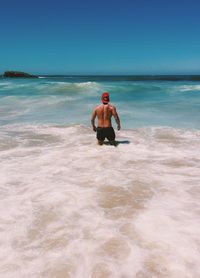 Rear view of shirtless man standing in sea against clear sky