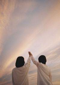 Rear view of couple standing against sky during sunset