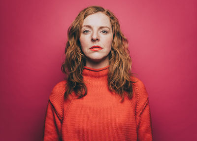 Portrait of confident woman in orange top over pink background