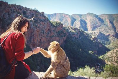 Young woman with monkey sitting on rock against clear sky