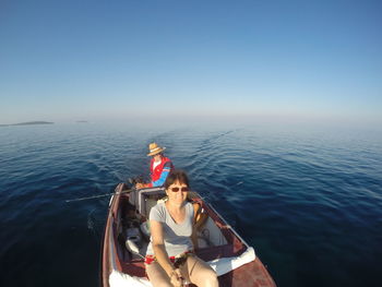 People on boat in sea against clear blue sky