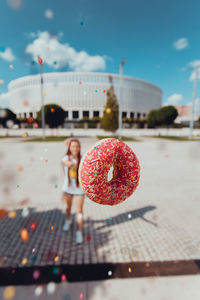 Donut in mid-air with young woman standing in background on walkway