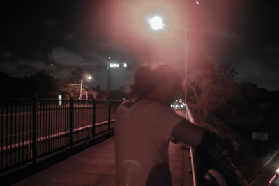 Rear view of man walking on illuminated street at night