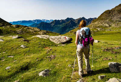 Rear view full length of female hiker standing on grassy field against sky