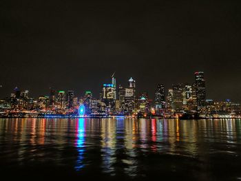 Illuminated buildings by river against sky at night