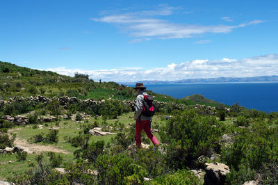 Backpack man hiking on mountain by sea against cloudy sky 