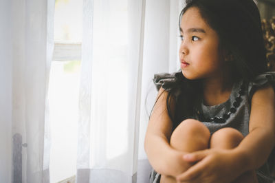 Woman looking away while sitting on window at home