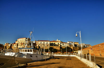 Sailboats moored at harbor by buildings against blue sky