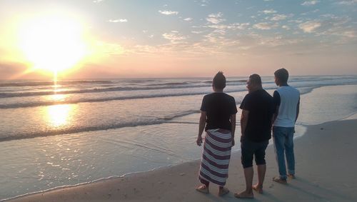 Rear view of friends standing at beach during sunset