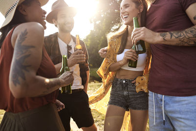 Cheerful friends toasting beer bottles at park