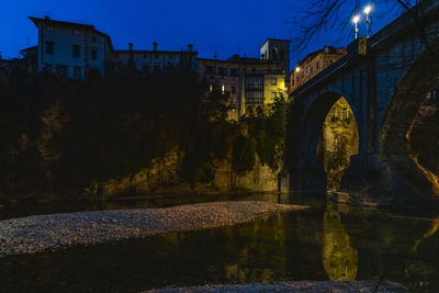 Arch bridge over lake by buildings against sky at night