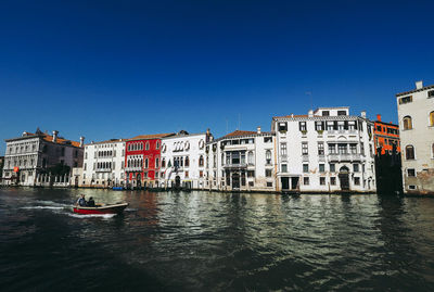 Canal by buildings against clear blue sky