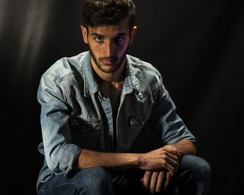 Portrait of young man sitting against black background