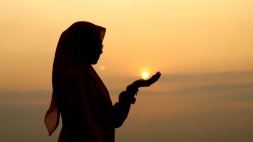 Silhouette woman standing against orange sky during sunset