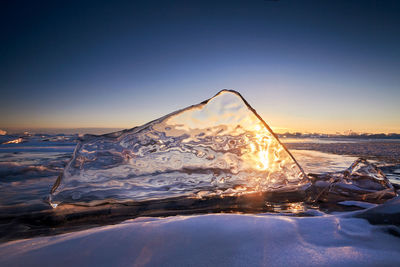 Snow covered land by sea against clear sky during sunset