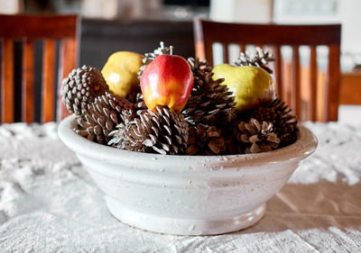 Close-up of fruits with pine cones in bowl on table