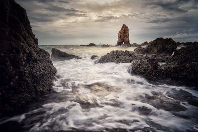 Waves splashing on rocks at shore against sky