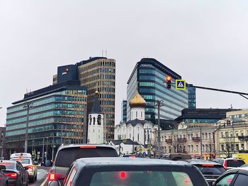 Vehicles on road by buildings against clear sky