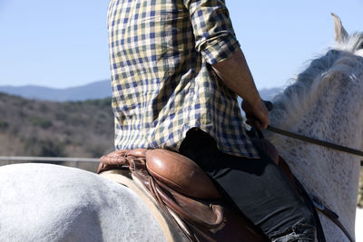 Midsection of man sitting on horse against sky