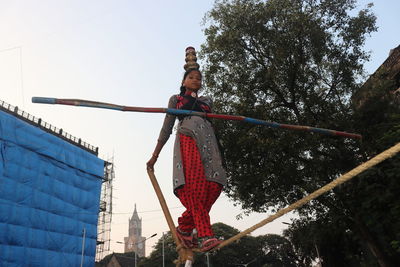 Low angle photograph of a young tightrope walker with pots on her head