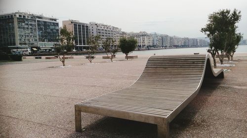 Empty bench by street in city against sky