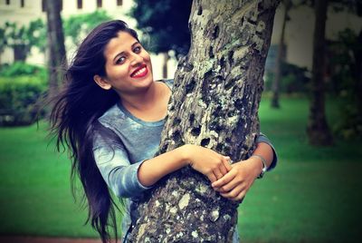 Smiling young woman against tree trunk