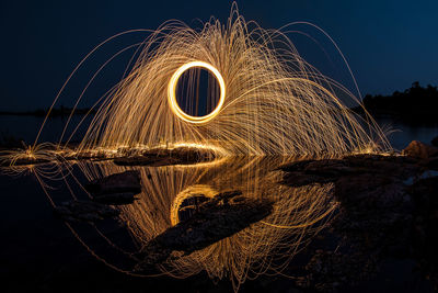 Wire wool reflection in water on shore against sky at night