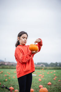 Portrait of young woman with arms raised standing on field against clear sky