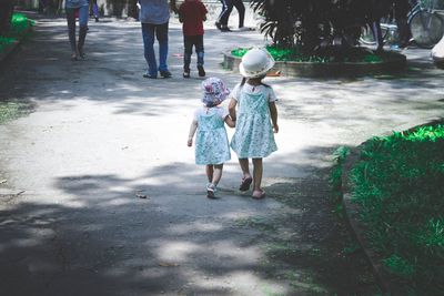 Rear view of sisters holding hands while walking on footpath