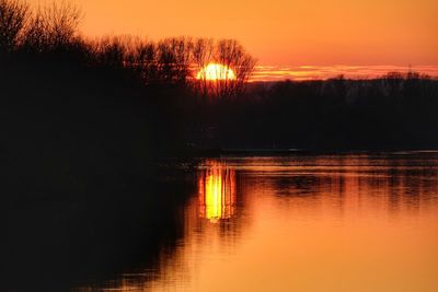 Silhouette trees by lake against romantic sky at sunset