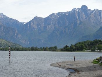 Woman standing on field by lake against mountains