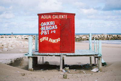 Red cabin at beach against sky