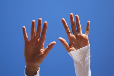 Low angle view of cropped woman with arms raised against clear blue sky