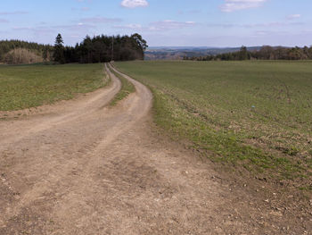 Dirt road amidst field against sky